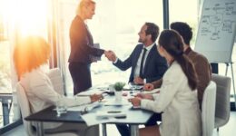 Handshake, success and contract with business people in meeting for deal merger, acquisition and thank you. Teamwork, loan agreement and banking firm with employees in office with lens flare