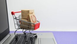 Shopping cart with purchases - packages and boxes on the modern laptop on trendy purple background. Online shopping and sale concept.