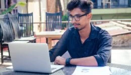 handsome and successful indian man in a stylish well-dressed freelancer working with a laptop on the beach.freelance and remote work.businessman student in a summer cafe on the shore of india ocean
