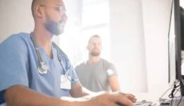 Serious doctor filling in electronic document with data of patient by computer