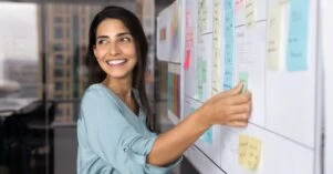 Smiling Latina professional woman placing sticky notes on planning board