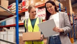 Female Team Leader With Clipboard In Warehouse Training Intern Standing By Shelves